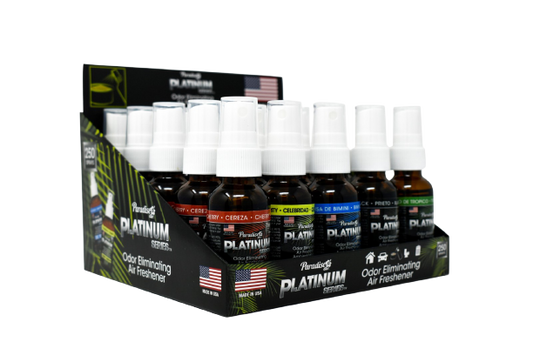 This is a display containing multiple bottles of "Paradise Platinum Series" odour eliminating air fresheners. Each bottle has a specific scent, some of which are visible like "Cherry" and "Black". The display packaging emphasises that these are made in the USA and are designed to eliminate odours.